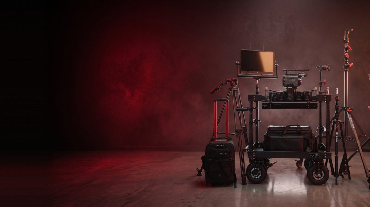 SHAPE camera cart with monitor and cinema camera, light stands, tripod, rolling backpack and gear bags against dark red smoke